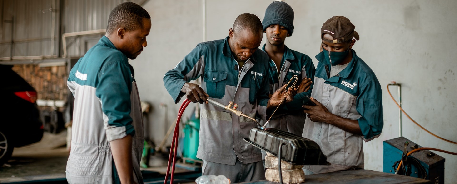 four workers fixing a vehicle part